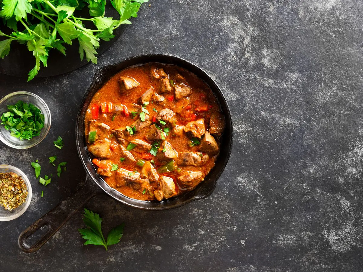 Cast-iron skillet of meat and vegetable stew with fresh herbs on a dark background