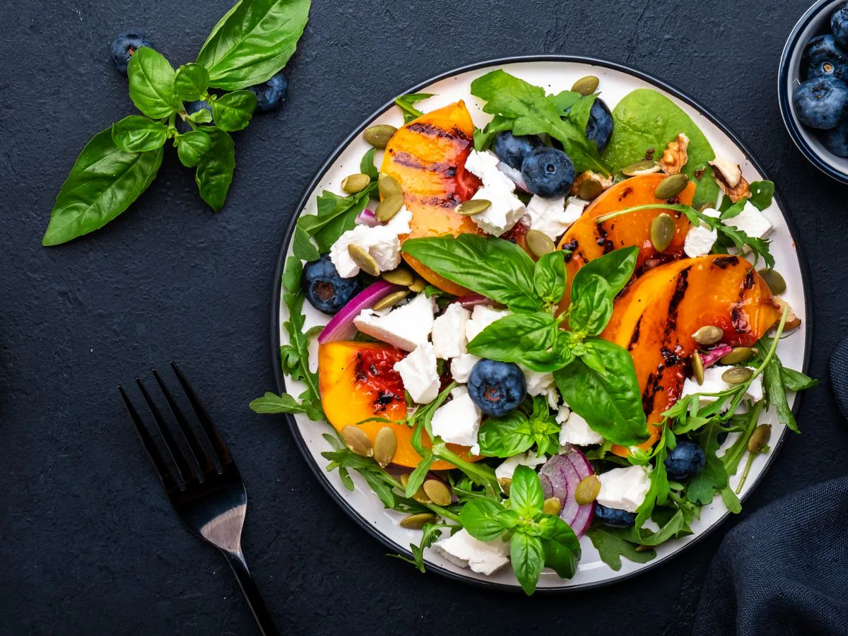 Salad with grilled squash, blueberries, feta cheese, pepitas, and basil on a dark table with a fork